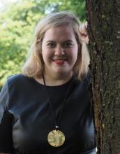 A head-and-shoulders portrait of a woman with blonde hair wearing black clothing, looking directly at the camera. 