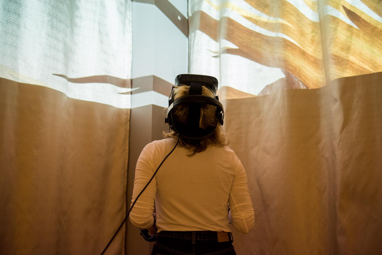 Ein weibliche Person mit VR-Brille legt ihren Kopf in den Nacken, oben im Bild erscheint eine Lichtinstallation.