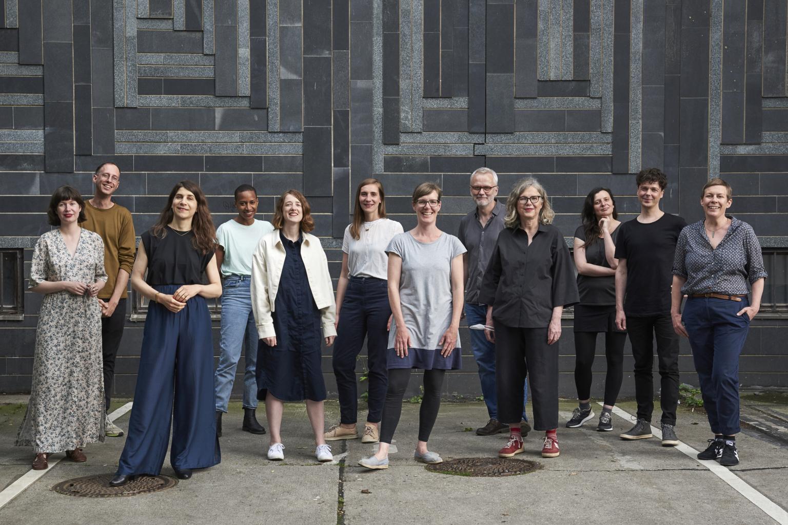 Teamfoto der Auswahlkommission vor einer Hauswand, alle Mitglieder blicken in die Kamera und lächeln.