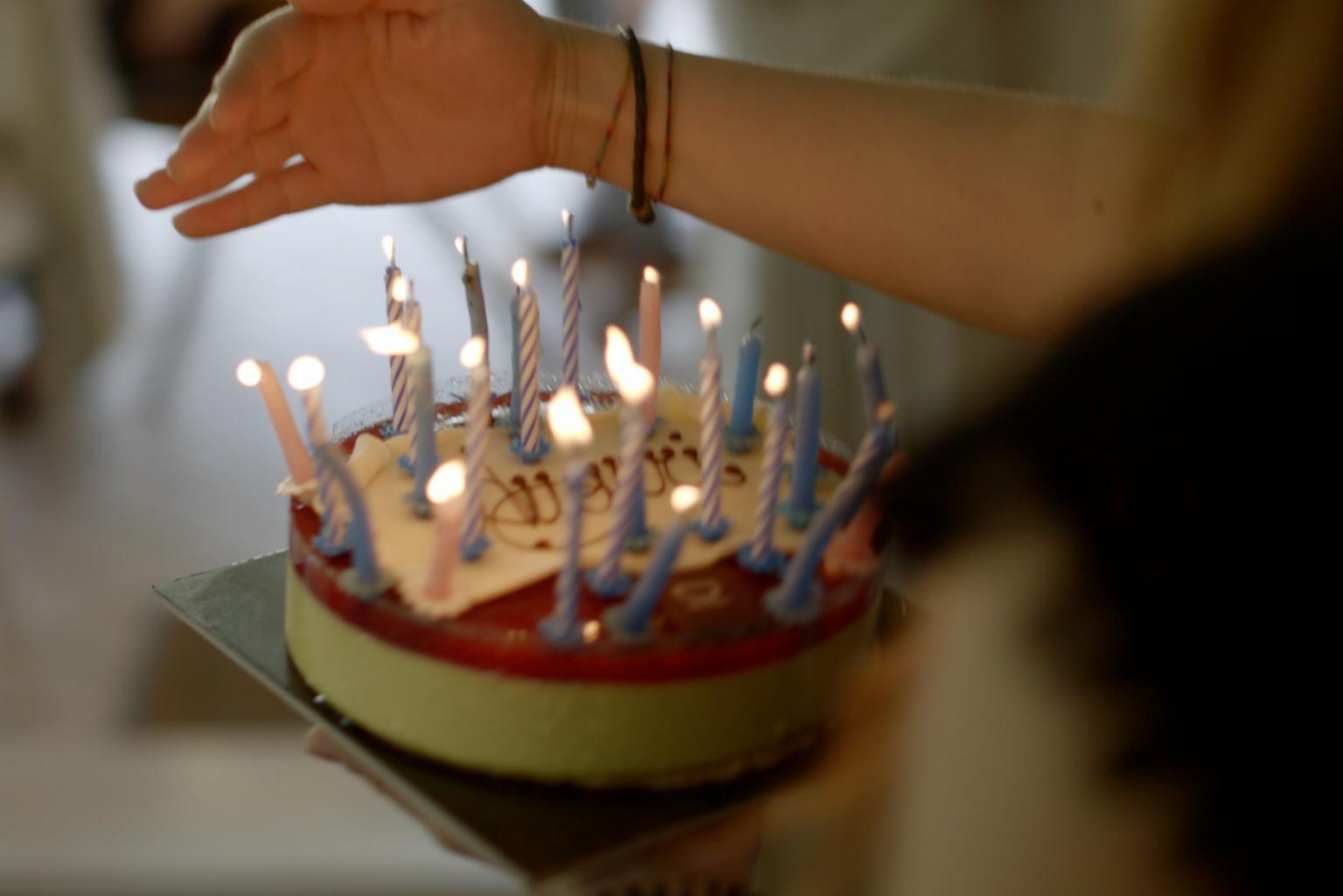 Eine Hand trägt eine Geburtstagstorte mit vielen brennen Kerzen darauf.