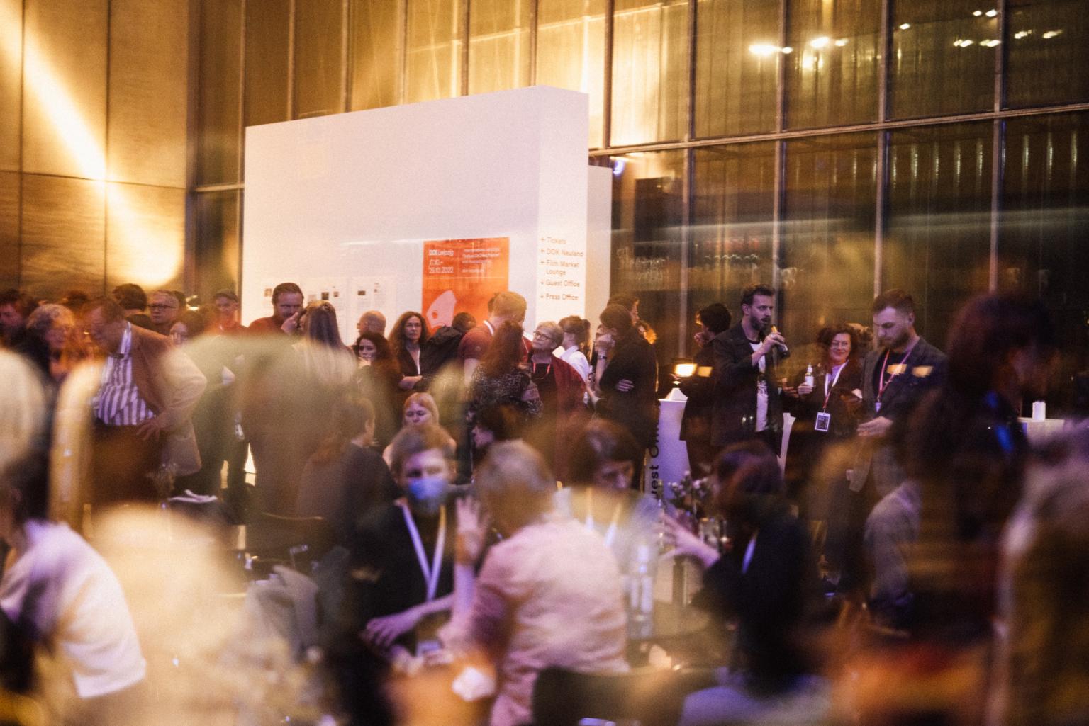 Lots of people stand, sit and talk in small groups at a festival reception.