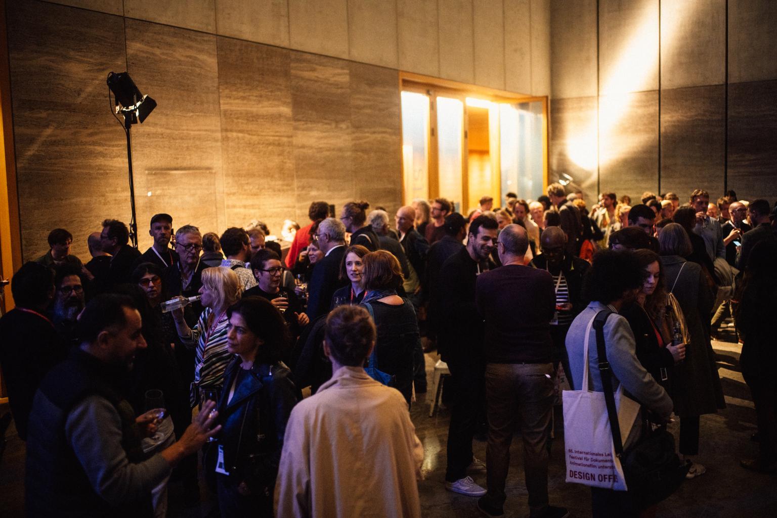 A lot of people stand, talk and drink in the huge hall of the Museum of Fine Arts in Leipzig.