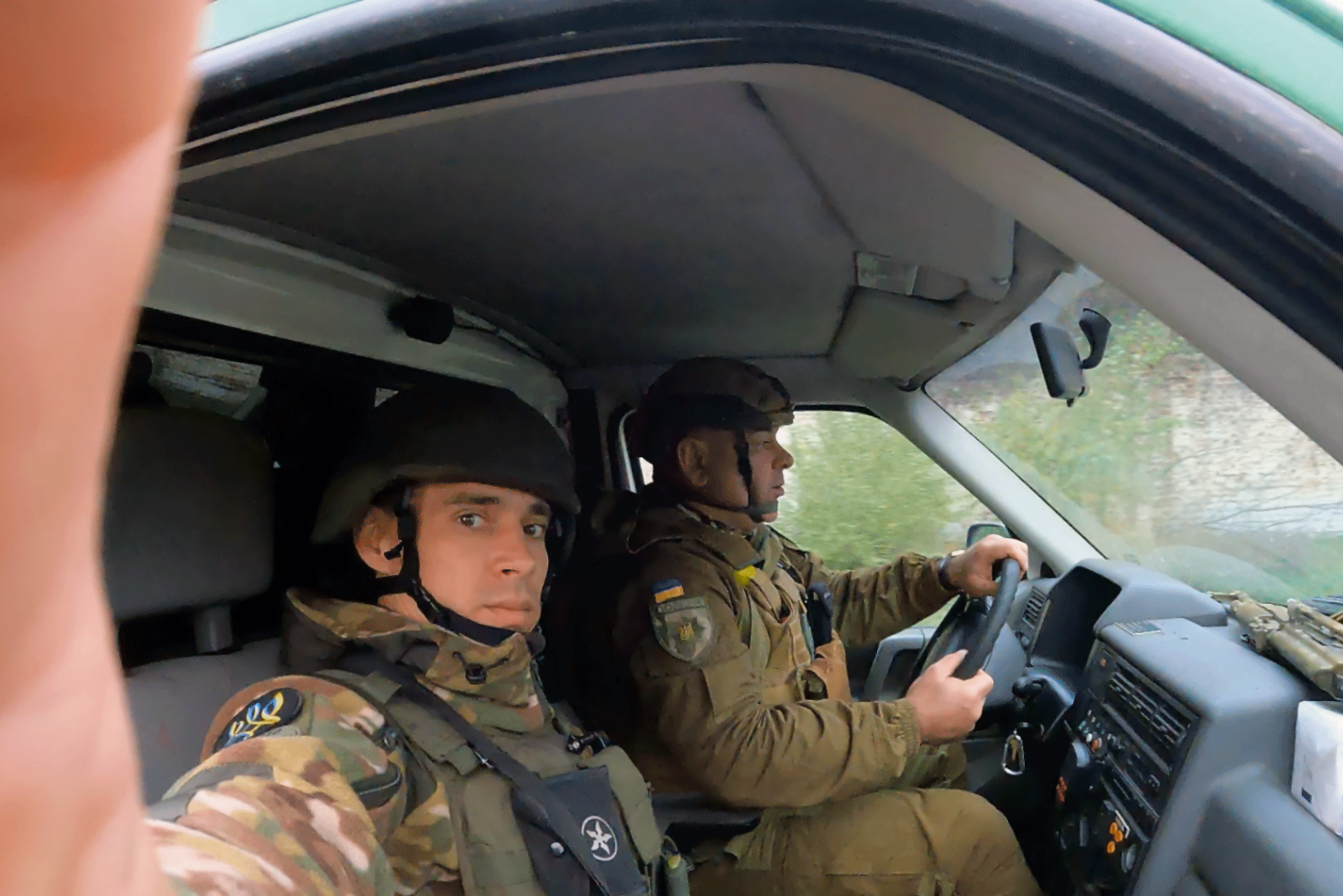 Zwei Soldaten in Uniform mit ukrainischer Flagge sitzen in einem Auto.