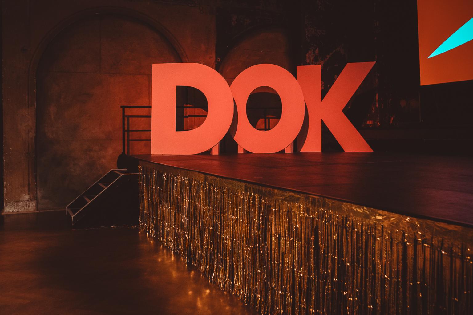 Drei große Pappbuchstaben DOK stehen auf einer Bühne, die mit Lametta dekoriert ist.