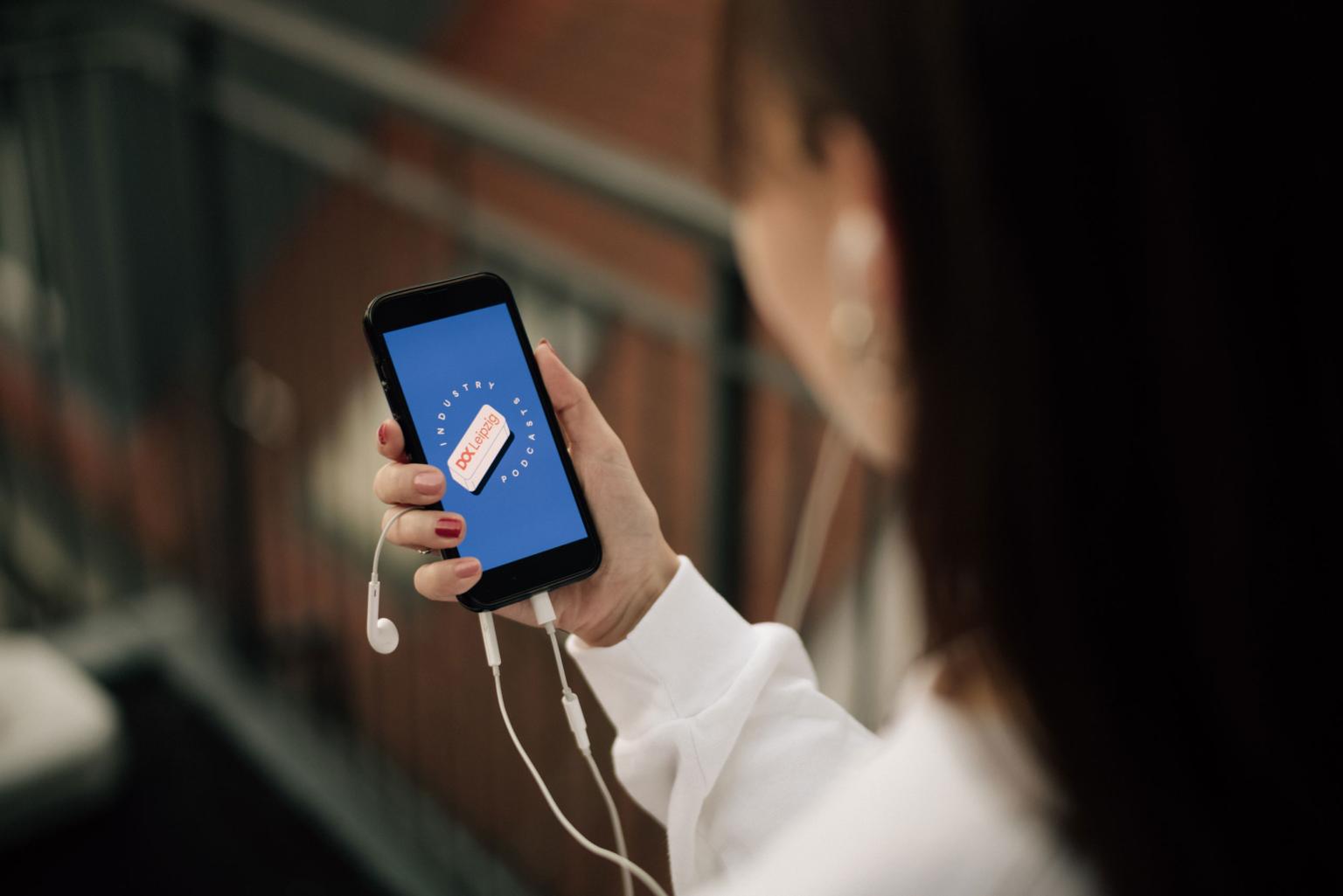A person is holding their phone and headphones up, the screen shows the Doc Industry podcast logo