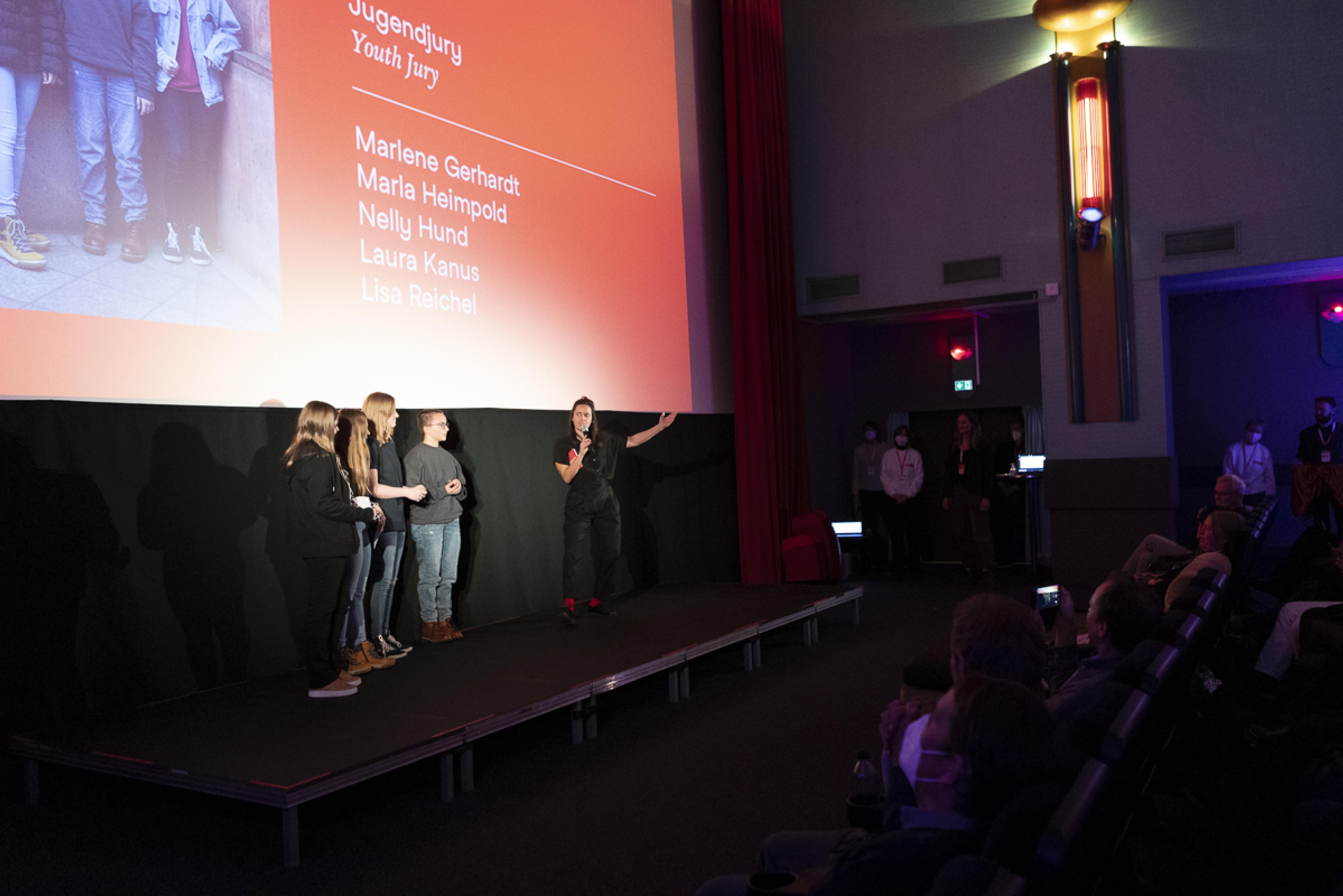 Bei der Verleihung der Partnerpreise: Moderatorin Julia Weigl stellt dem Publikum die vier Mitglieder der Jugendjury vor, die neben ihr stehen.