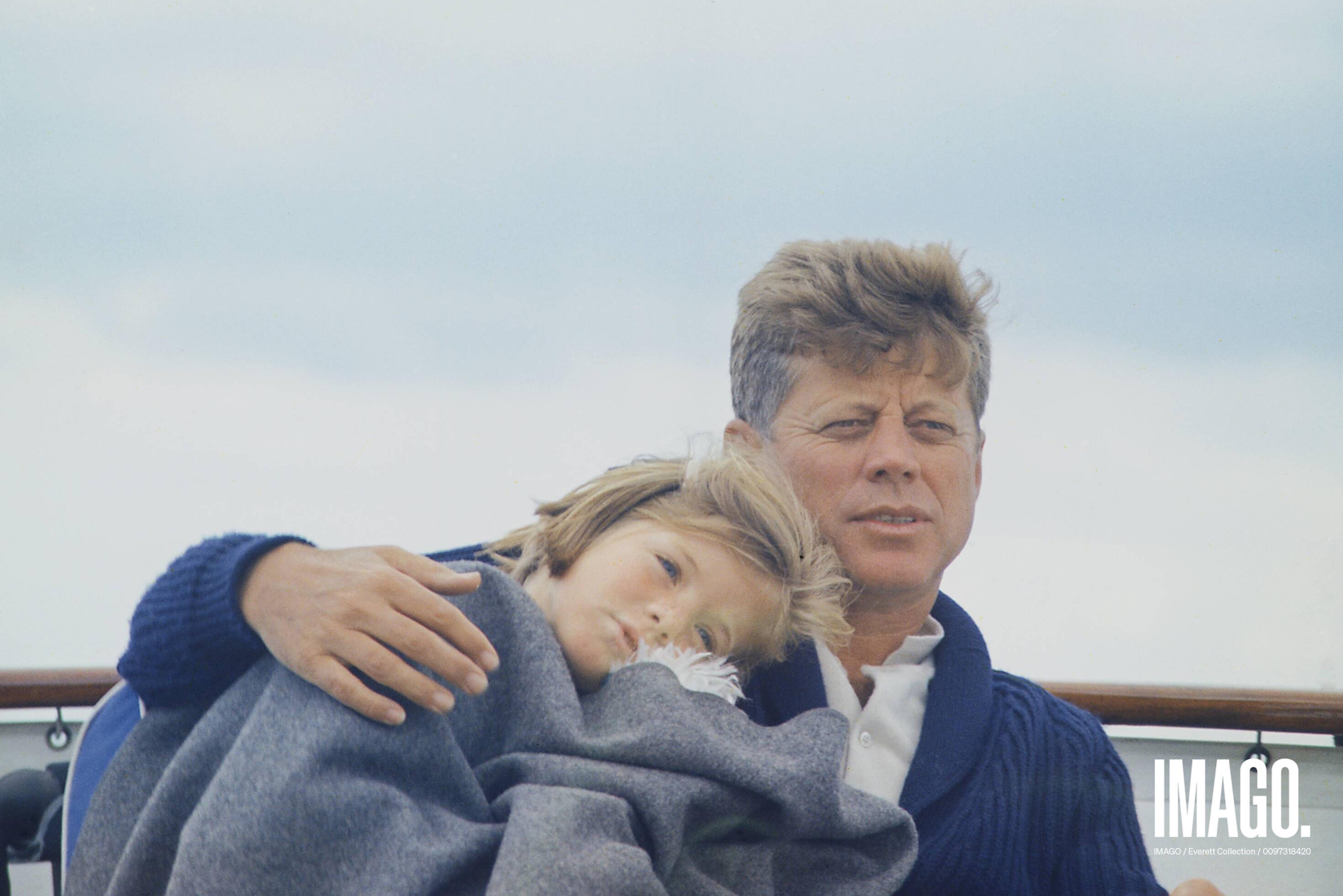 President John Kennedy with his daughter Caroline. He has his arm around her, they both look into the distance. 