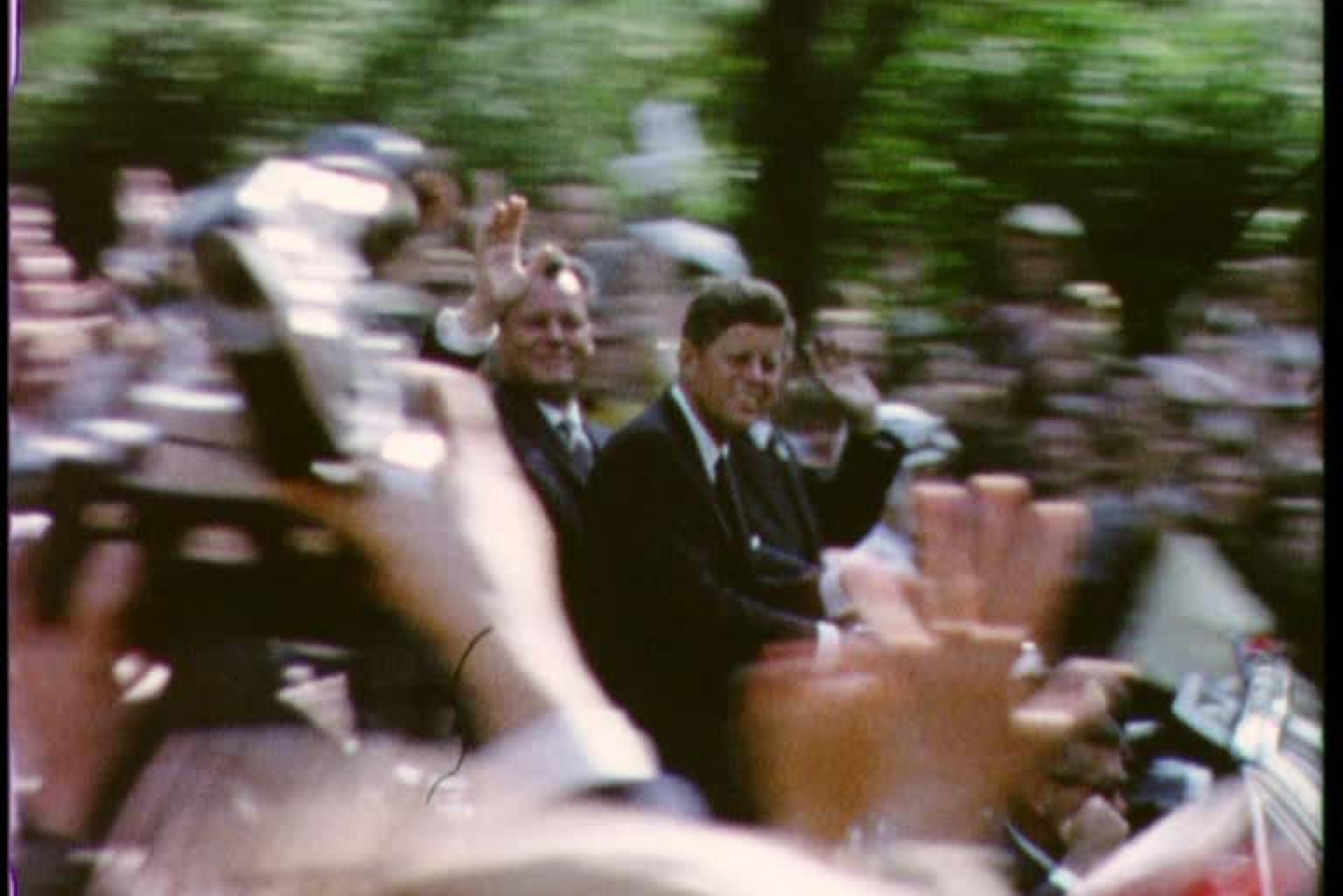 Willy Brandt and John Kennedy riding together in an open car and waving through a crowd of people.