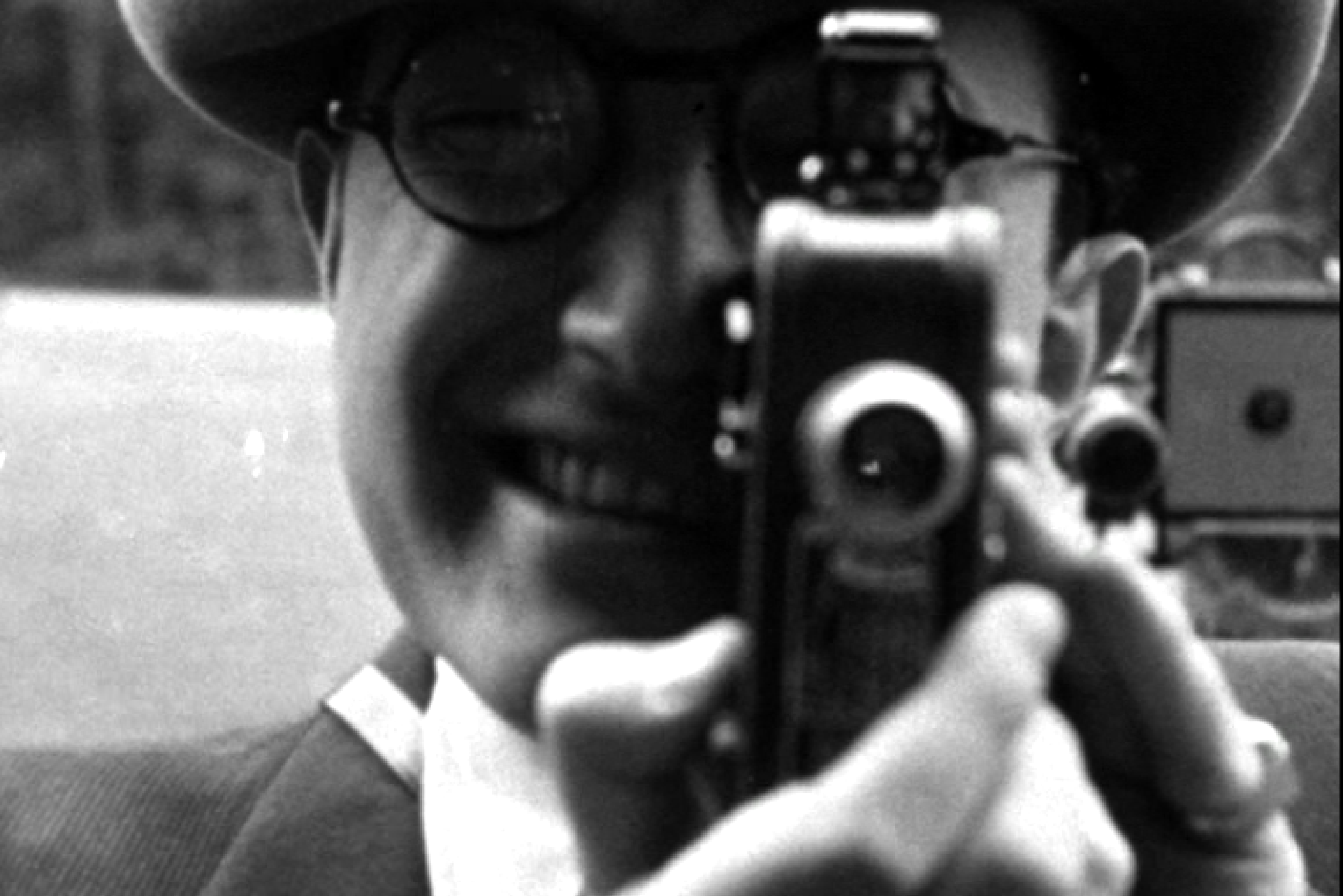 Black and white photo: A man smiling looks through the viewfinder of a historic N8 camera.