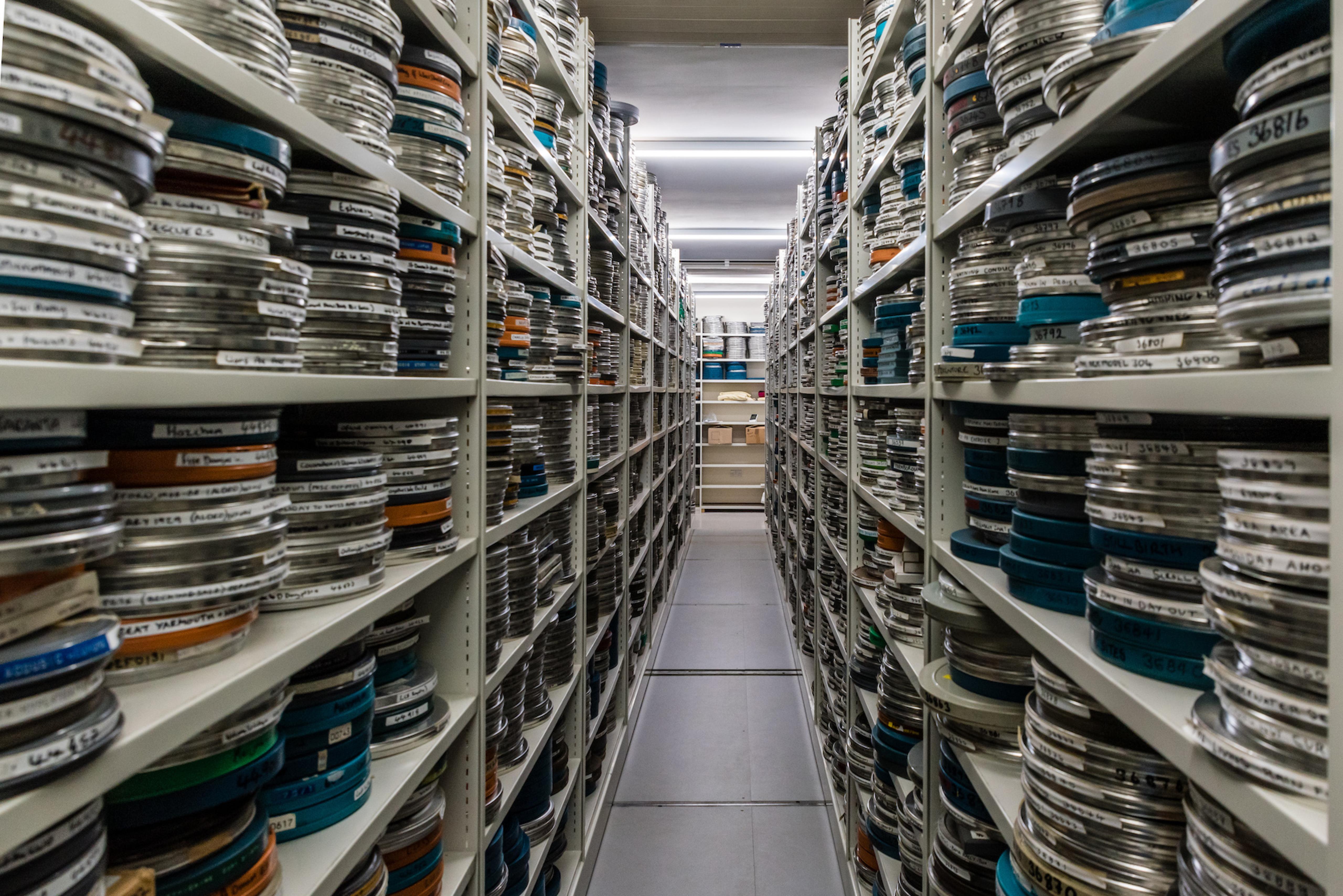 A room with high steel shelves stacked with numerous rolls of film