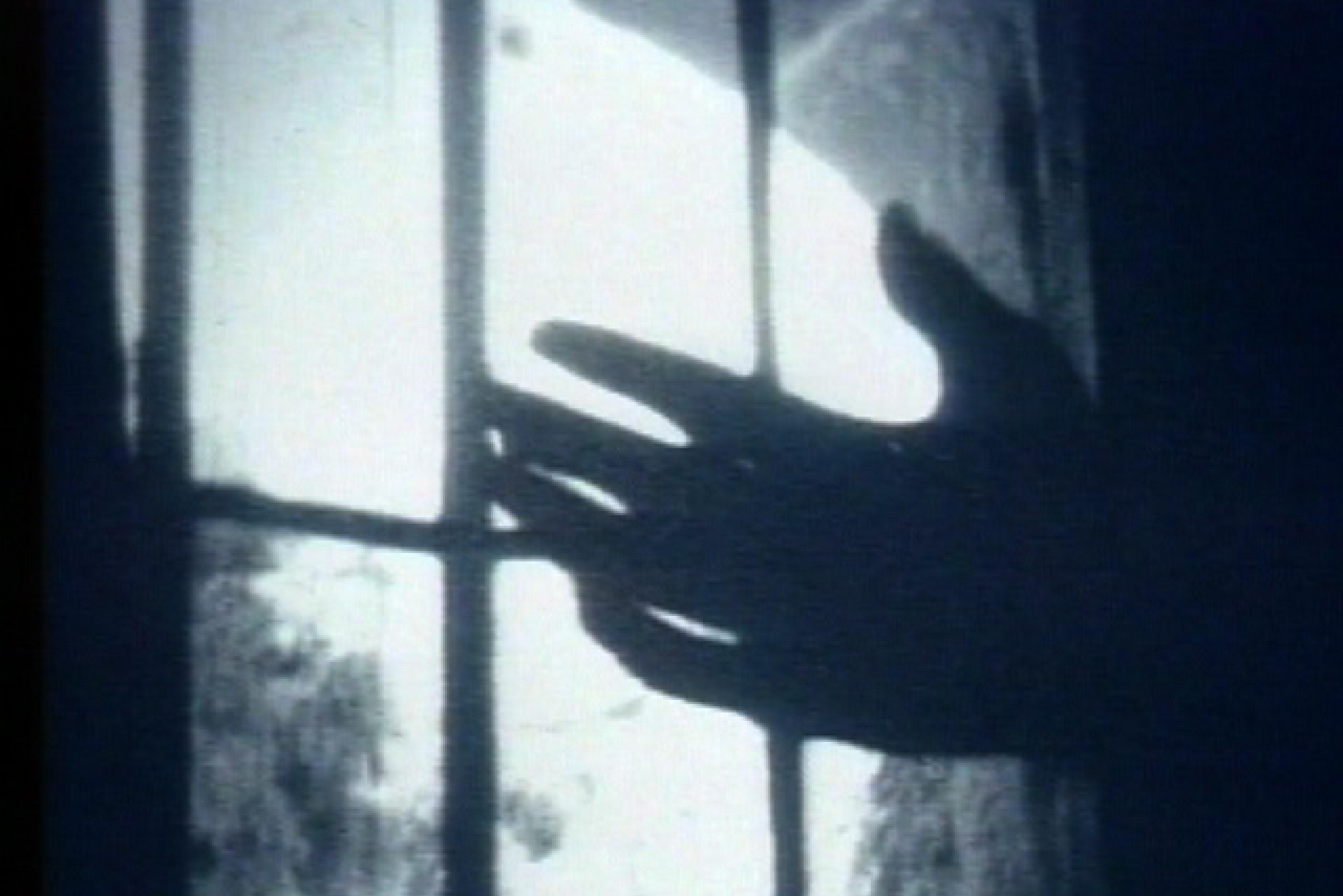 Black and white: Close-up of an open hand in front of a prison window. 