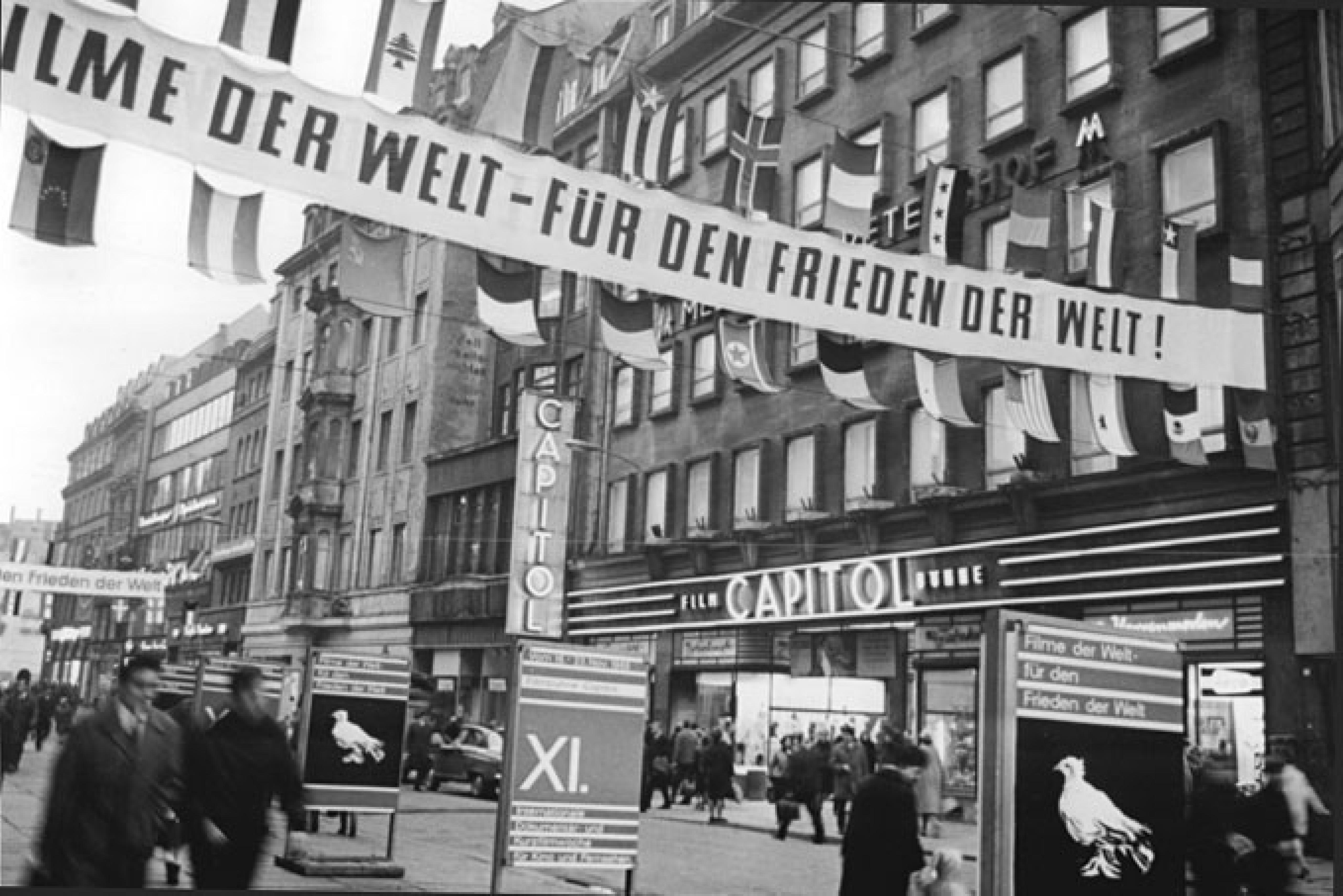 Die Petersstraße in Leipzig. Über der Straße hängt ein Banner mit dem Text "Filme der Welt für den Frieden der Welt".
