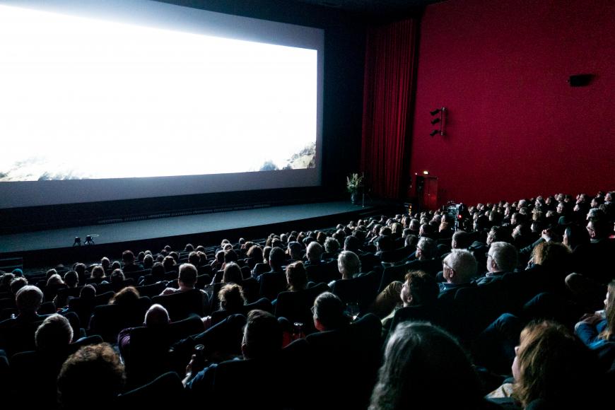 Cinema full of visitors who are looking to a white screen.