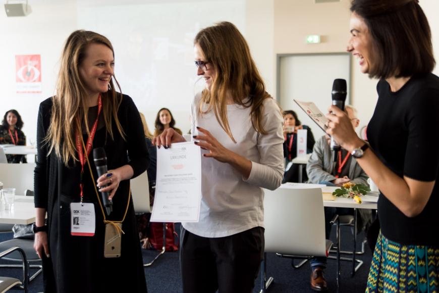 Three women standing side by side, the woman in the middle receives a certificate.
