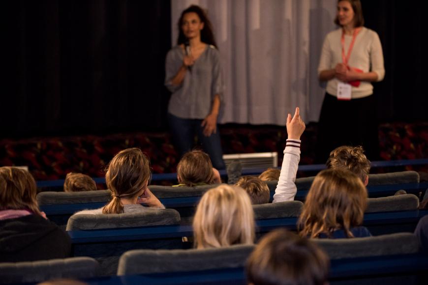 Blick von hinten über die Zuschauerreihen in einem Kinosaal, vorne bei der Leinwand  stehen zwei Frauen mit Mikrofon in der Hand.