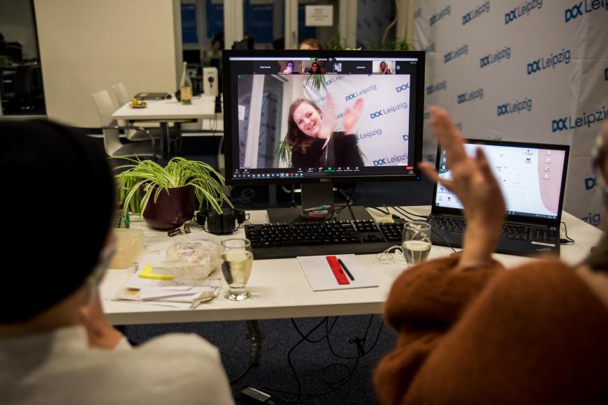 Ein Tisch mit einem Computerbildschirm, auf dem Brigid O'Shea jubelnd zu sehen ist. Auch im Vordergrund sind klatschende Hände zu sehen