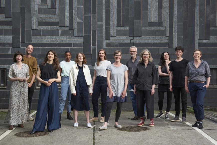 Teamfoto der Auswahlkommission vor einer Hauswand, alle Mitglieder blicken in die Kamera und lächeln.