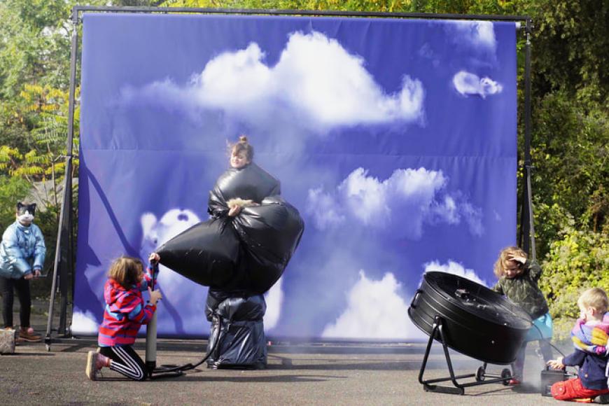 Fünf Kinder drehen in einem Filmset, im Hintergrund eine Leinwand mit Abspann, rechts steht eine Windemaschine.
