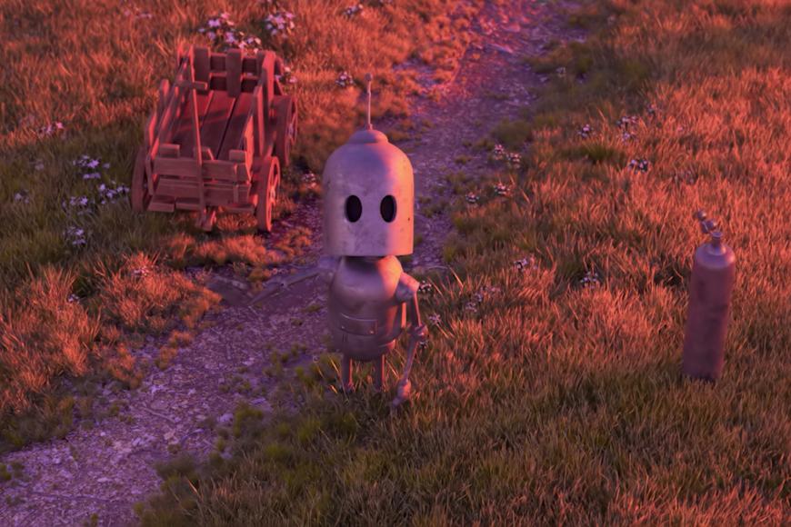 Ein blecherner Roboter steht am Rand eines schmalen Trampelpfads auf dem Gras und schaut direkt zum Zuschauer. Neben ihm steht ein Holzkarren
