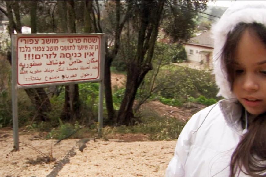 Filmszene aus "Once I entered the Garden": Ein Mädchen in einer Winterjacke blickt auf den Boden, neben ihm steht ein Hinweisschild in hebräischer und arabischer Schrift.