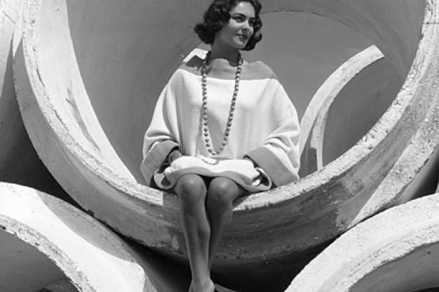 Archivbild: Eine Frau im Minikleid und großer Perlenkette sitzt in einem großen Rohr.