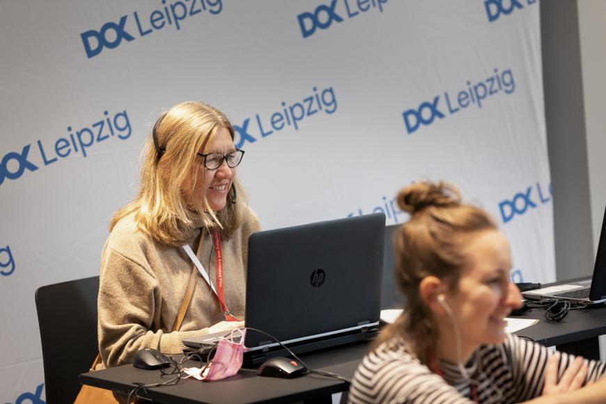Nadja Tennstedt (director of DOK Industry) and Ulrike Schmidt (coordinator Co-Pro Market) are sitting in front of their laptops, earphones plugged in, and both are smiling.