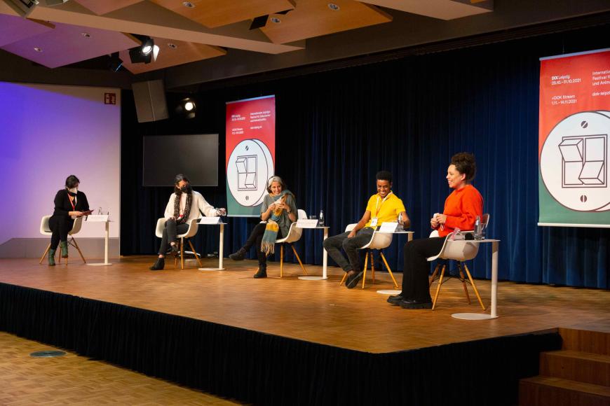 Fünf Personen auf einem Talk-Podium bei DOK Leipzig, darunter vier Frauen und Ein Mann. Alle lachen miteinander.