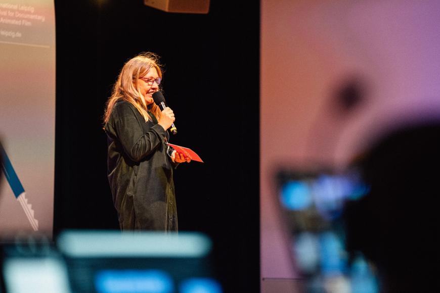 Director of Dok Industry Nadja Tennstedt on stage. She speaks into a microphone and smiles slightly.