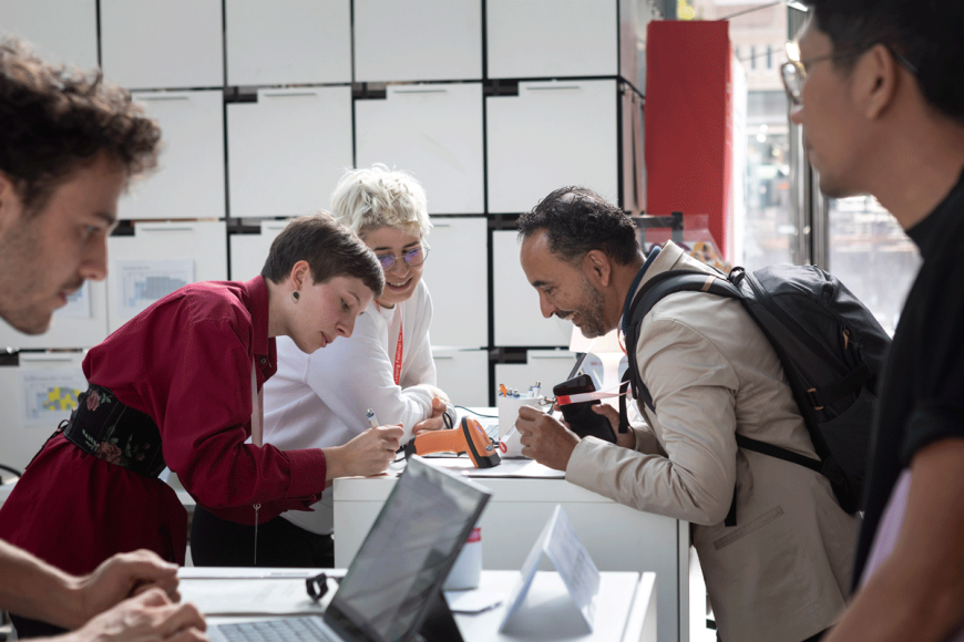Drei Personen beugen sich über einen weißen Schaltertresen und schreiben etwas auf. 