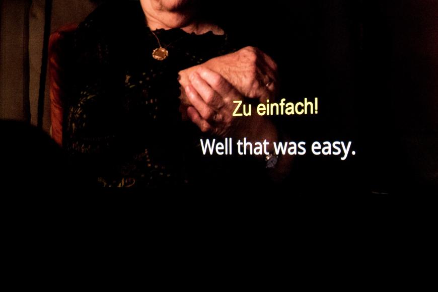 Eine Kinoleinwand mit zwei Untertitel-Reihen. Oben steht auf deutsch: Zu einfach! Und steht auf Englisch: Well that was easy.