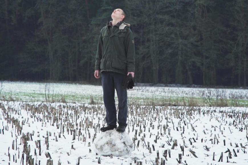 Ein junger Mann steht in einem mit Schnee bedeckten Stoppelfeld und blickt nach oben.