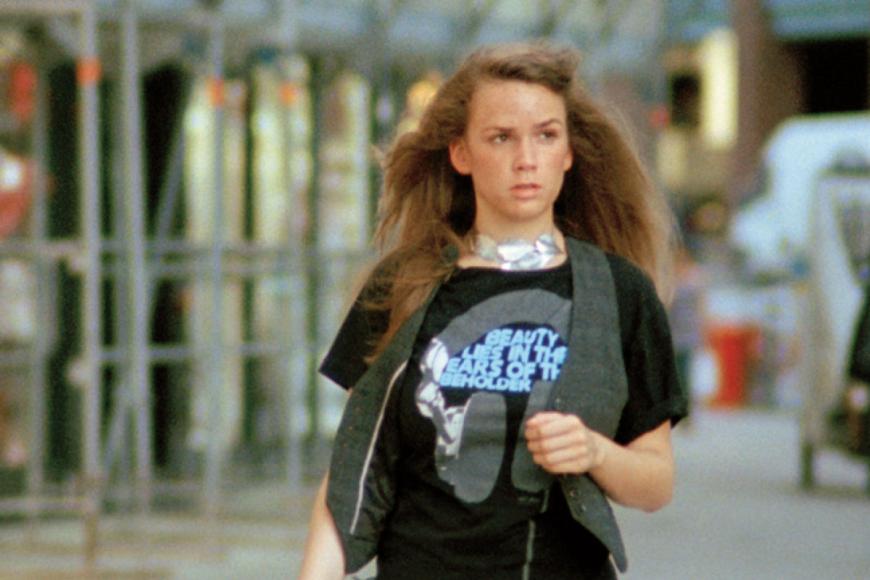 Eine junge Frau mit langen Haaren geht an Gebäuden entlang.