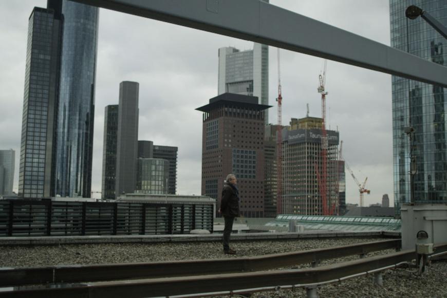 Ein Mann steht auf einem Gebäudedach inmitten der Skyline von Frankfurt.
