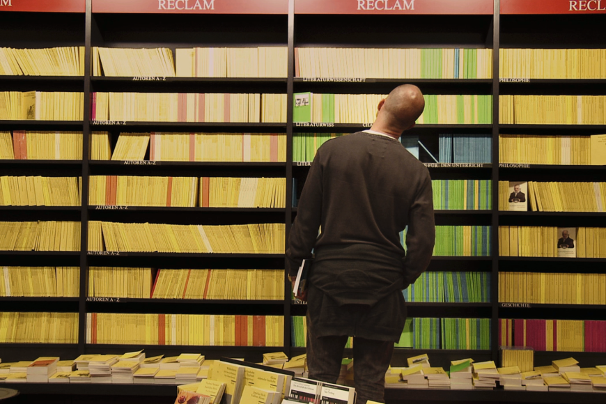 Ein Mann steht vor einem riesigen Bücherregal voll mit Reclam-Heften.