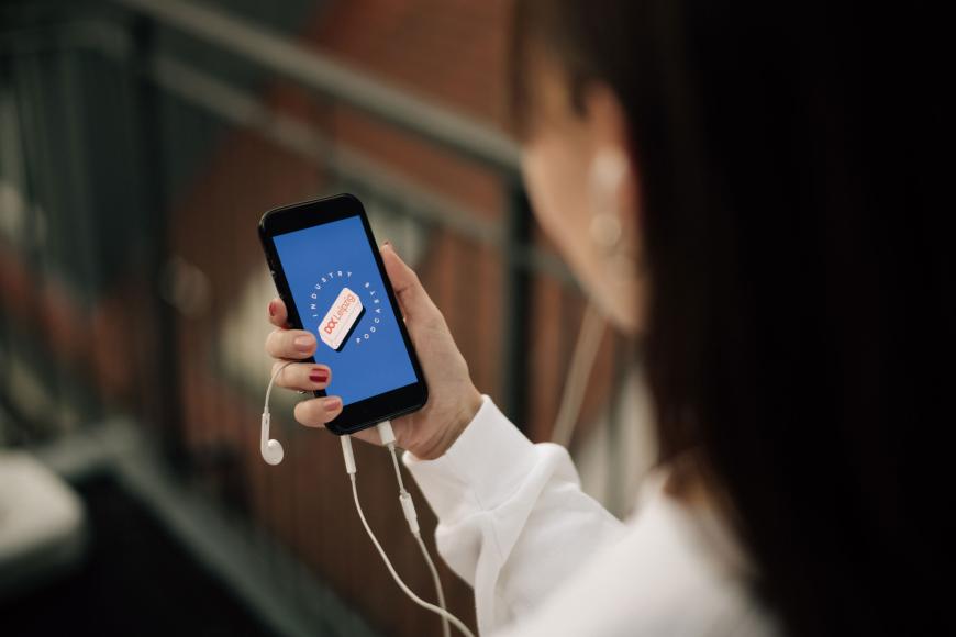 A person is holding their phone and headphones up, the screen shows the Doc Industry podcast logo