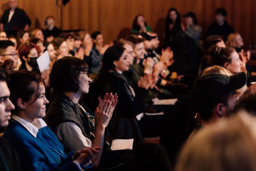 The audience is clapping their hands and smiling towards the stage
