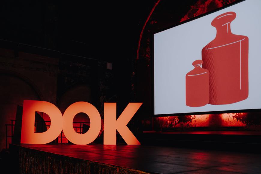 Die Bühne der Preisverleihung mit drei angestrahlten menschengroßen Pappbuchstaben: D, O und K. Auf der Leinwand prangt das Festivalmotiv von 20254, zwei rote Gewichte