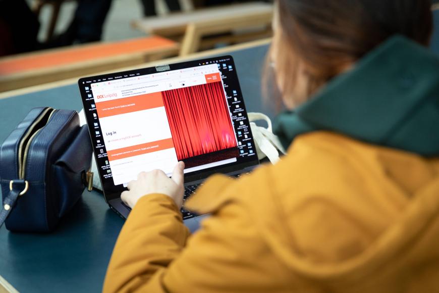 Ein industrygast in Gelber Jacke sitzt vor einem Laptop, das den Dok Leipzig Login Bildschirm